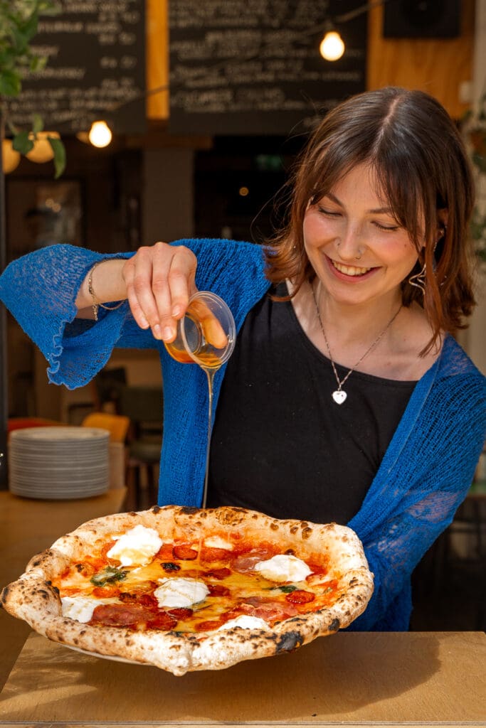 person pouring olive oil on top of authentic neapolitan pizza