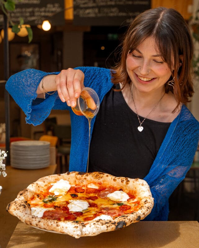 chilli oil being poured over napoli pizza by woman