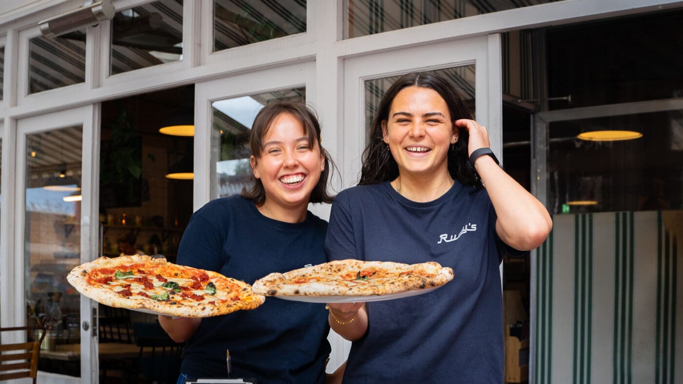 two girls holding neapolitan pizza and smiling