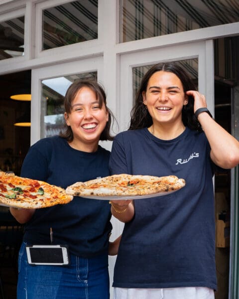 two waiters holding plates of authentic neapolitan pizza