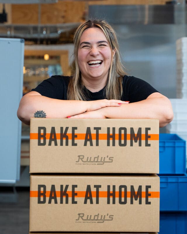 person near two boxes with pizzas to bake at home from rudy's