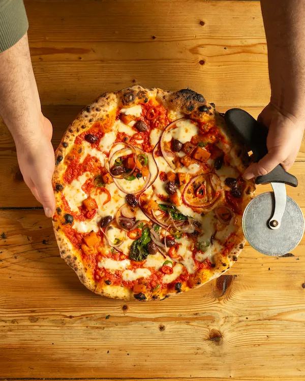 person holding pizza cutter wheel next to neapolitan pizza