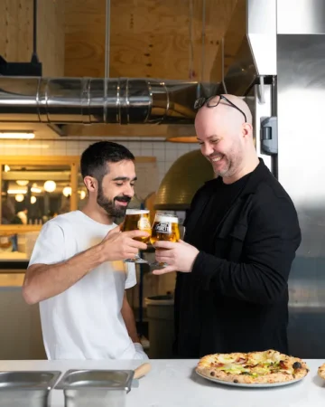 two people cheering with beer glasses and neapolitan pizza on the side